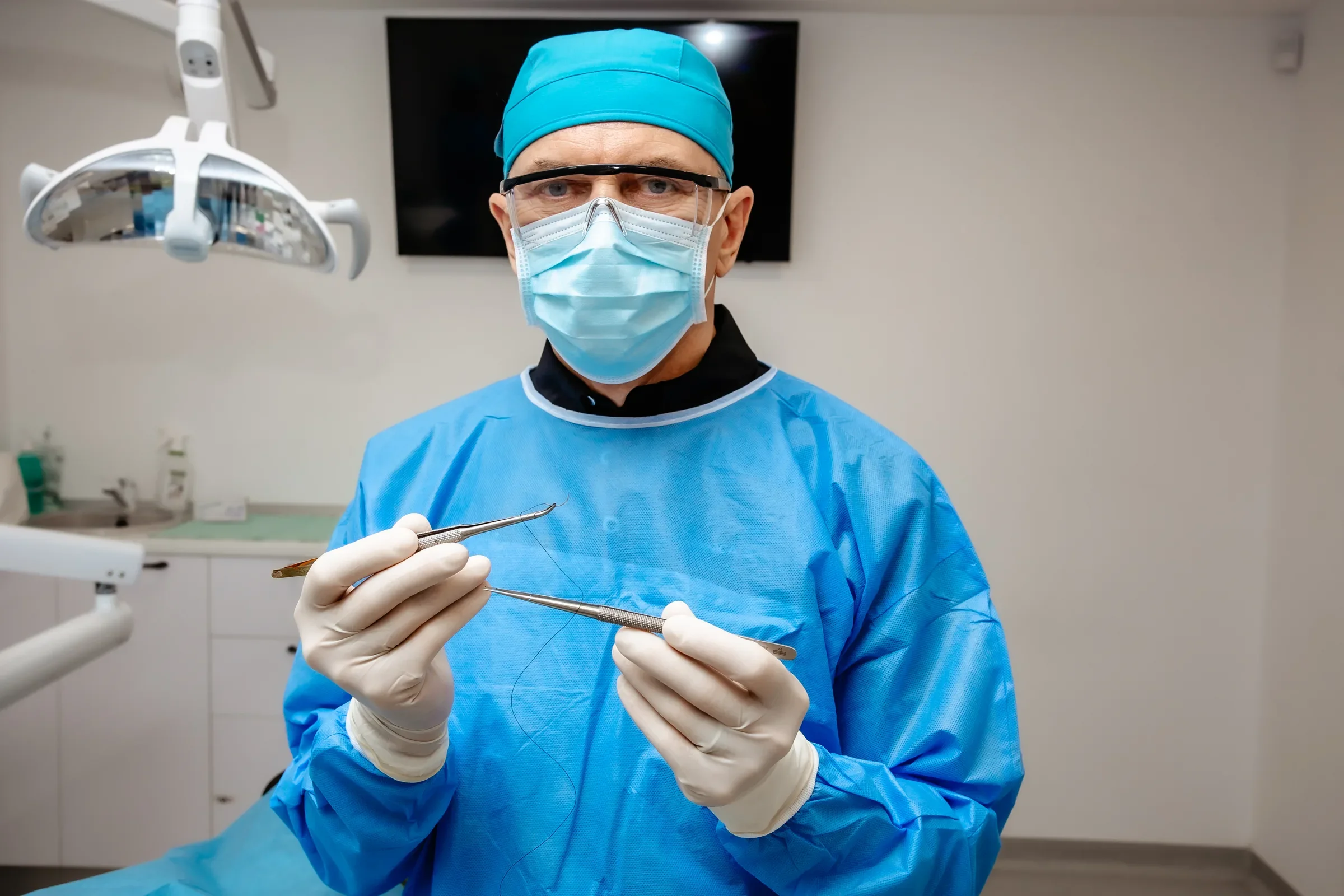 Medic SalvaDent în echipament chirurgical, cu portacul și fir de sutură în mâini, în cabinetul de tratament